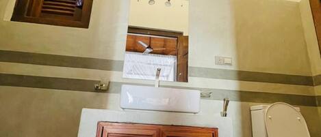 Un baño con puerta de madera, un lavabo blanco, un espejo y un ventilador de techo.