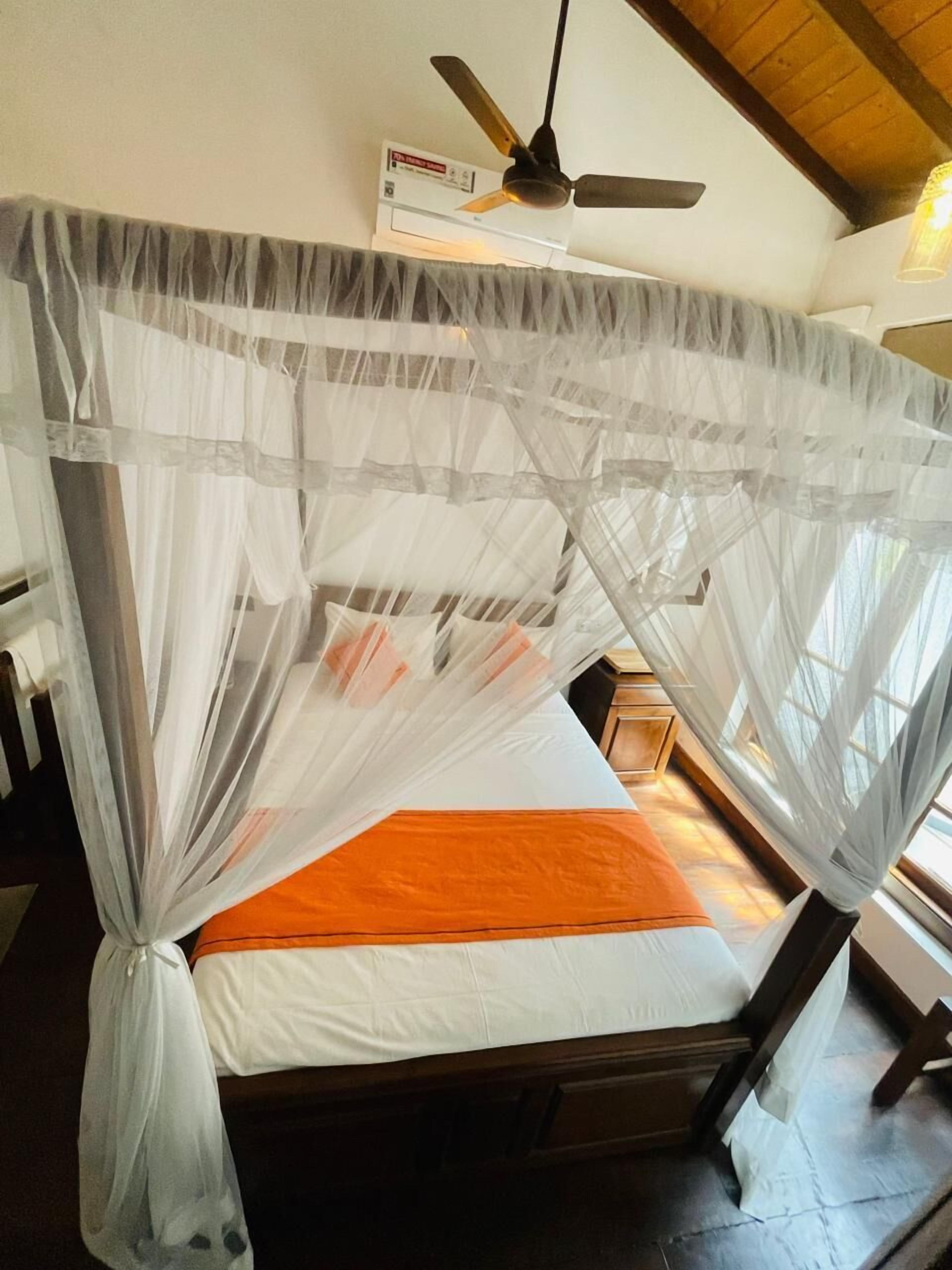 Una cama con mosquitero, ventilador de techo y un mueble en la pared.