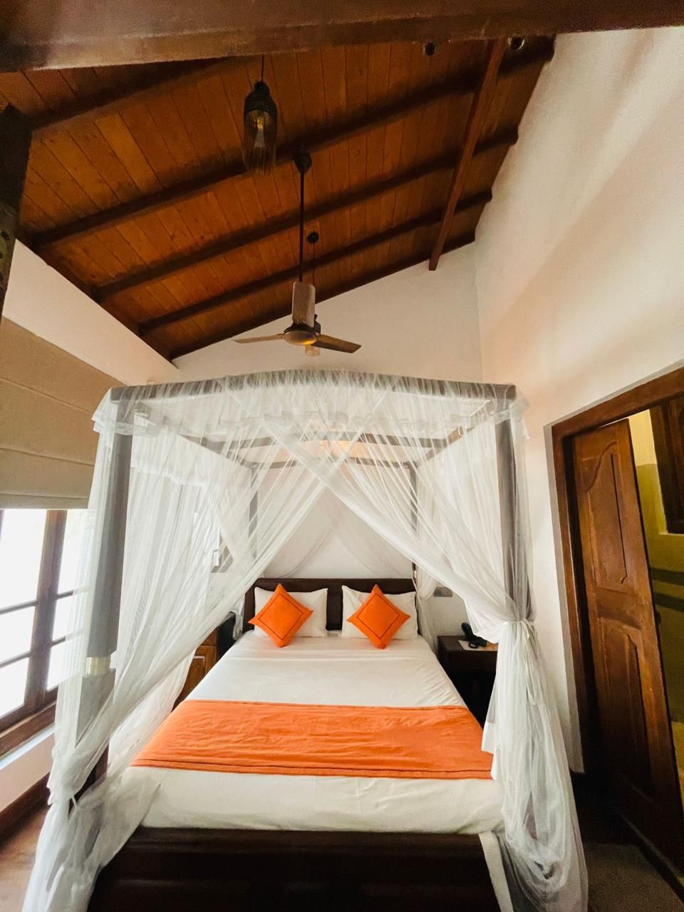 A bed with a canopy, two orange pillows, and a wooden ceiling.