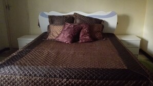 A bed with a quilted brown cover, two bedside tables, and a white headboard. - Christy Mwila Chisenga (Kitwe)