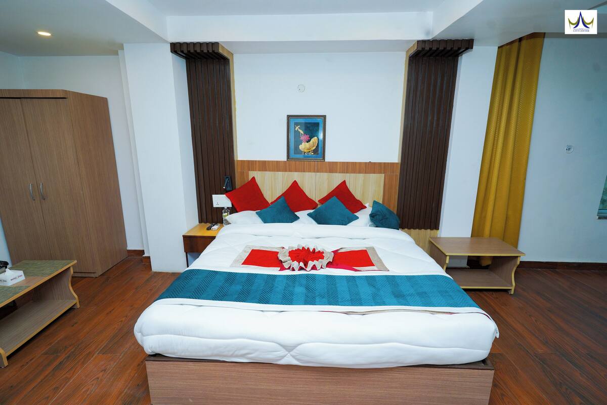 Quarto de hotel bem arrumado com uma cama grande, um guarda-roupa de madeira, uma mesa de cabeceira e uma pequena mesa.