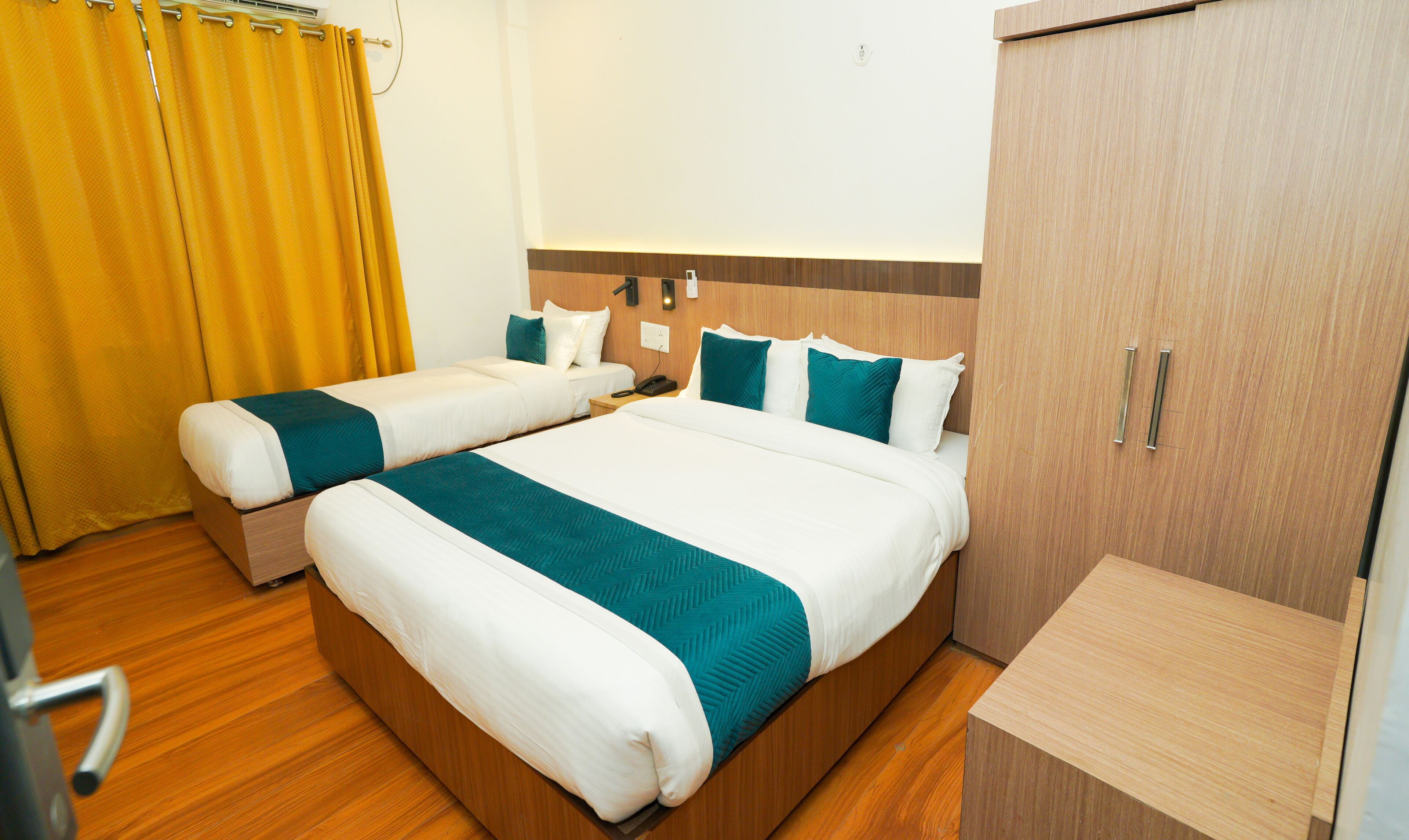 Una habitación de hotel con dos camas, un armario de madera, un escritorio y una cortina amarilla.