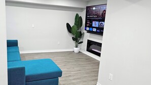 Un salon moderne avec un canapé d’angle bleu, un téléviseur à écran plat fixé au mur et une plante en pot.