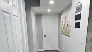 Un couloir doté d’un plancher en bois gris, de portes blanches et d’un luminaire encastré au plafond.