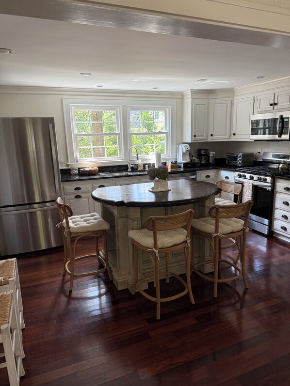 A kitchen with a central island, wooden chairs, a stainless steel refrigerator, and white cabinets.