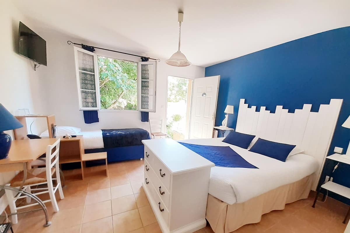 Quarto com cama, escrivaninha, cadeira, cômoda, televisão e janela com cortinas.