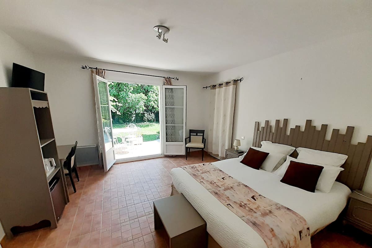 Quarto com cama, mesa de cabeceira e vista do jardim pela porta.