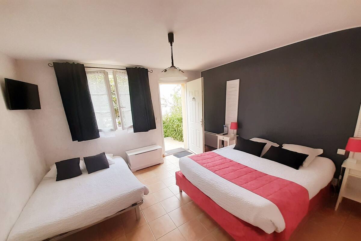 Quarto de hotel com duas camas, uma mesa, uma cadeira, televisão e janela com cortinas.