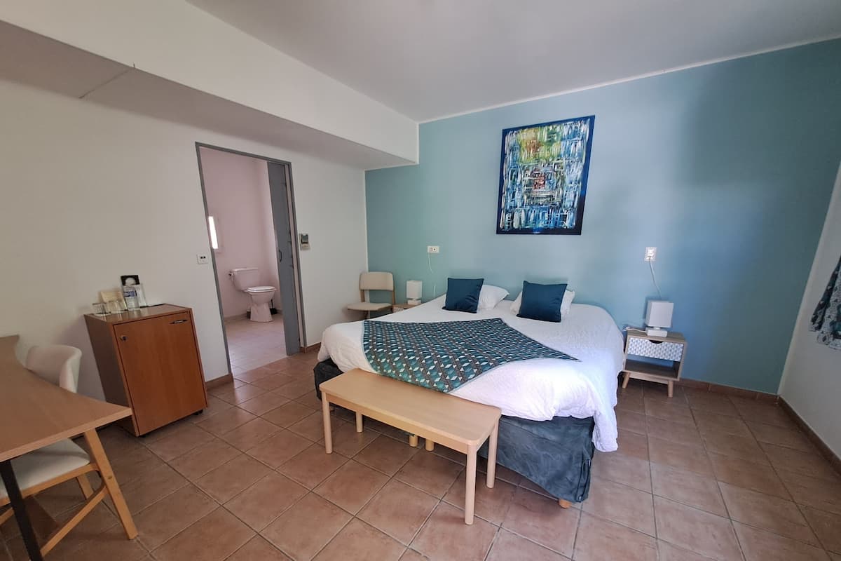 Quarto com cama, mesas de cabeceira, escrivaninha, cadeira, guarda-roupa e banheiro visível por uma porta aberta.