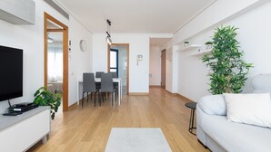 Una sala moderna con un televisor de pantalla plana, un comedor con sillas y una mesa, un sofá y una planta verde grande.