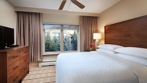 Une chambre d’hôtel avec un lit, une commode en bois, une télévision, une fenêtre avec des rideaux et une lampe.