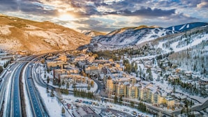 Une ville enneigée où se côtoient des bâtiments modernes et traditionnels, traversée par une autoroute et entourée de montagnes.