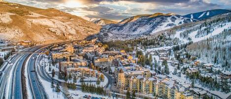 A snow-covered town with a mix of modern and traditional buildings, a highway, and surrounding mountains.