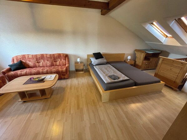 A cozy loft-style room with a sofa, a bed, a small table, and a wooden cabinet.
