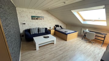 Una habitación estilo loft con techo inclinado, una cama, un sofá, una mesita y un escritorio con una silla.