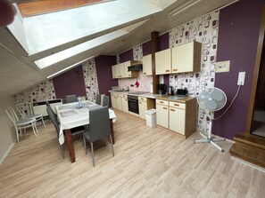 A compact kitchen with a dining area, a ceiling fan, and a small trash bin.