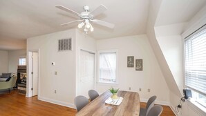 A dining area with a wooden table, grey chairs, a ceiling fan, and a window with blinds. - Cityscape Escape (Cincinnati)