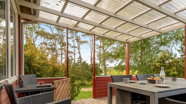Un patio exterior con una zona de estar techada, terraza de madera y vistas del paisaje circundante.