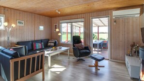 Interior acogedor de una cabaña con techo de madera, un sofá, una mesa de comedor y una silla.