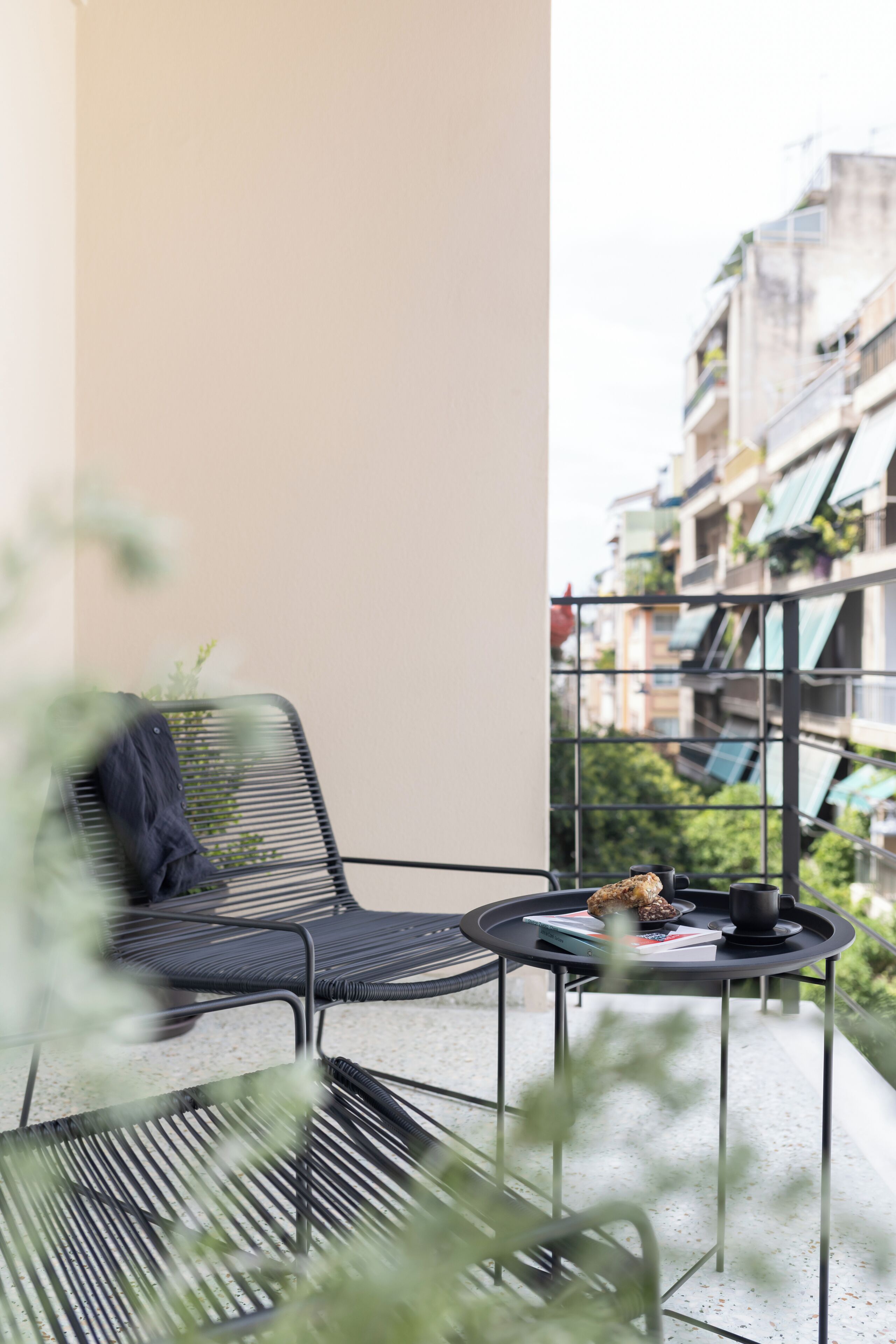 En balkong med en stol och ett litet bord, med utsikt över ett bostadsområde med byggnader och grönska.