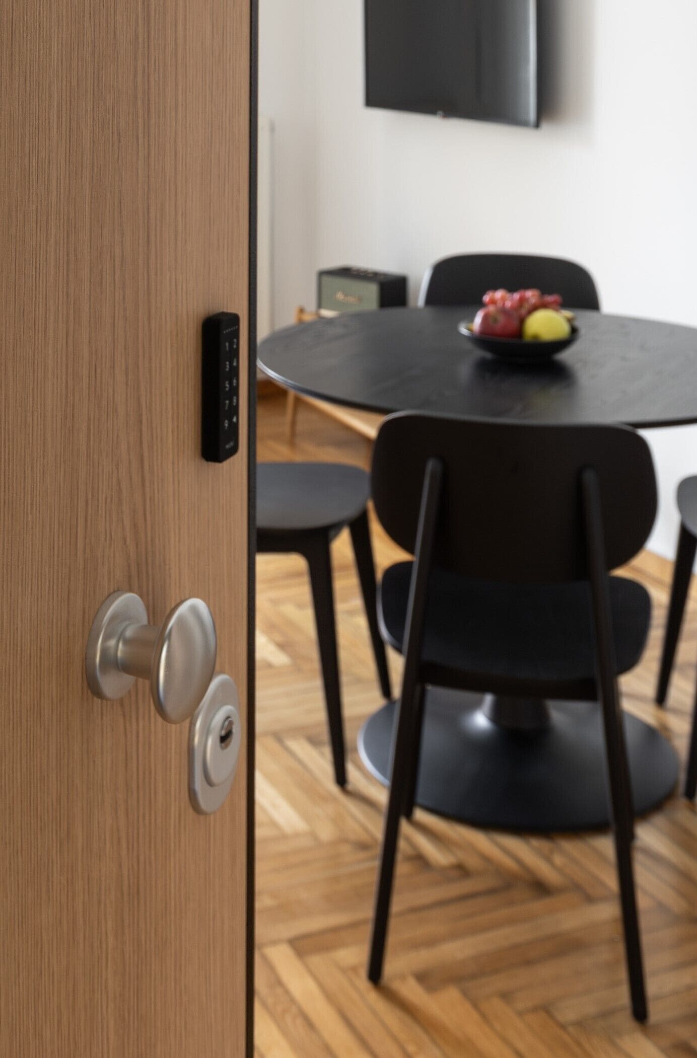 Una habitación moderna con puerta de madera, una mesa redonda con sillas y un televisor de pantalla plana en la pared.