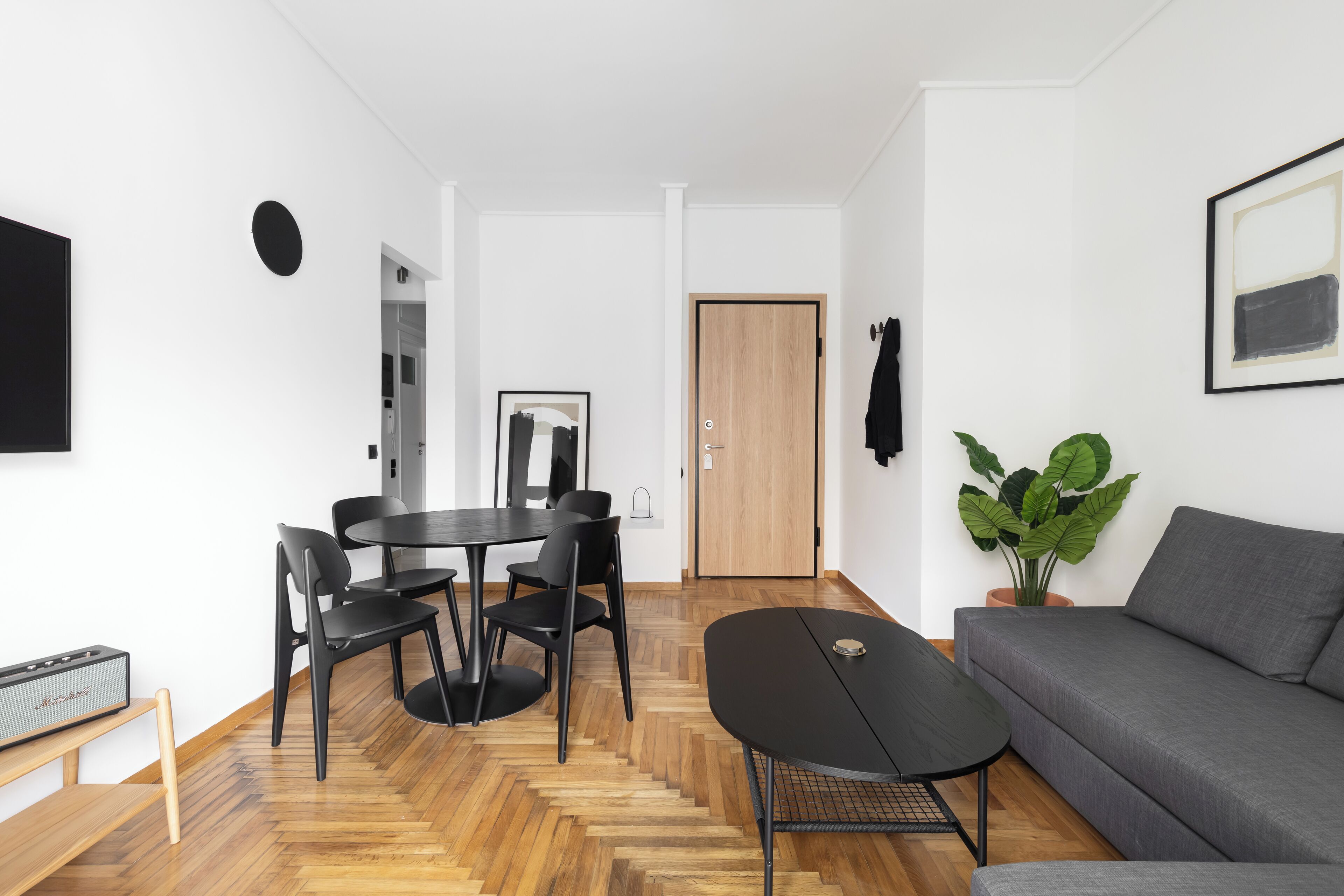 Een moderne woonkamer met een grijze bank, een ronde eettafel met zwarte stoelen, een zwarte salontafel en een houten visgraatvloer.