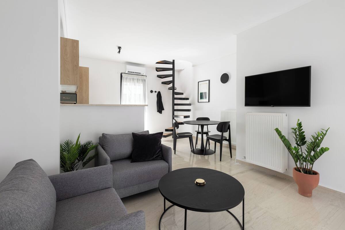 A modern living room with a grey sofa, a round black coffee table, and a TV mounted on the wall.