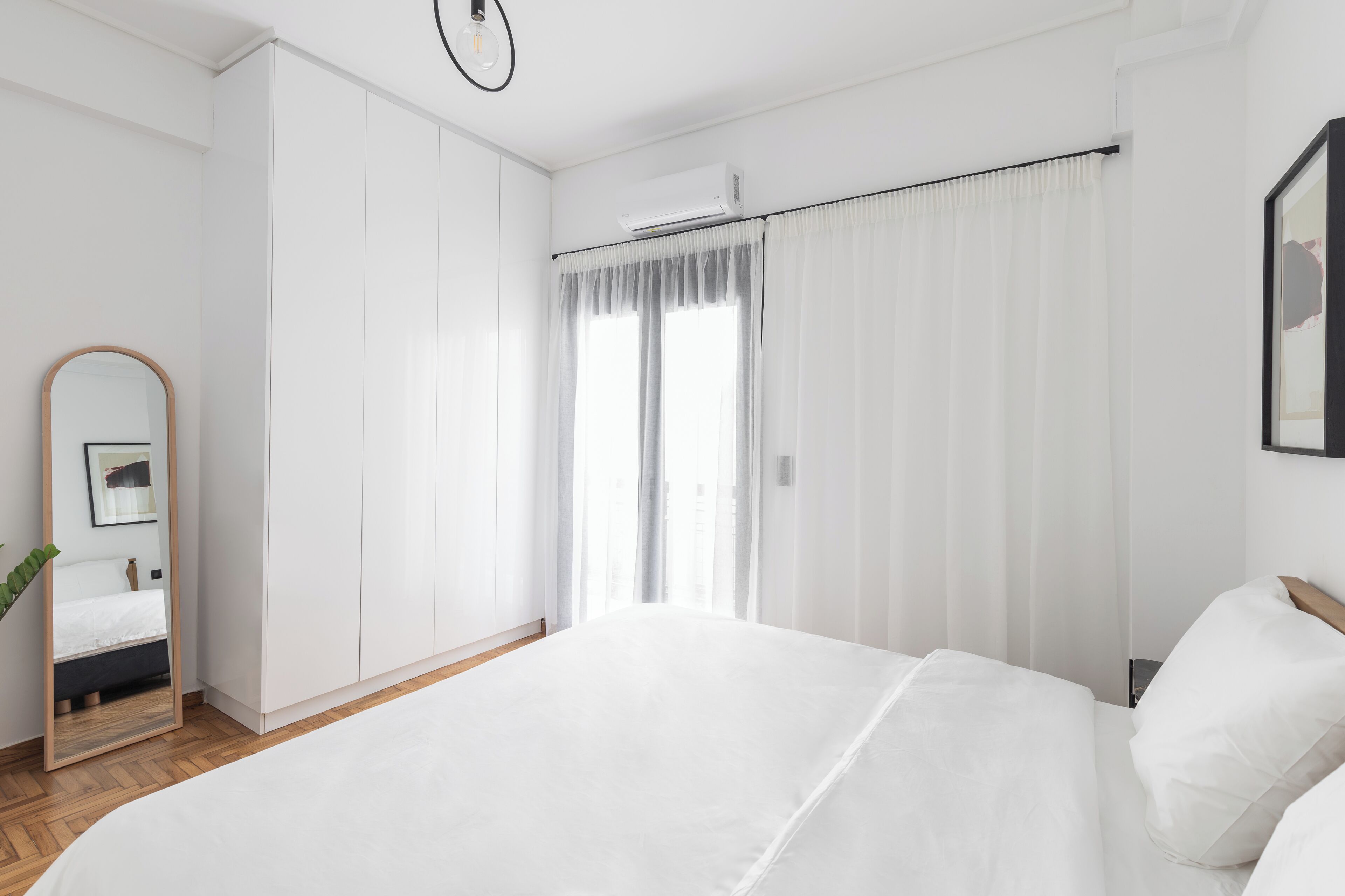 Une chambre à coucher avec un grand lit, un miroir et une fenêtre avec des rideaux.