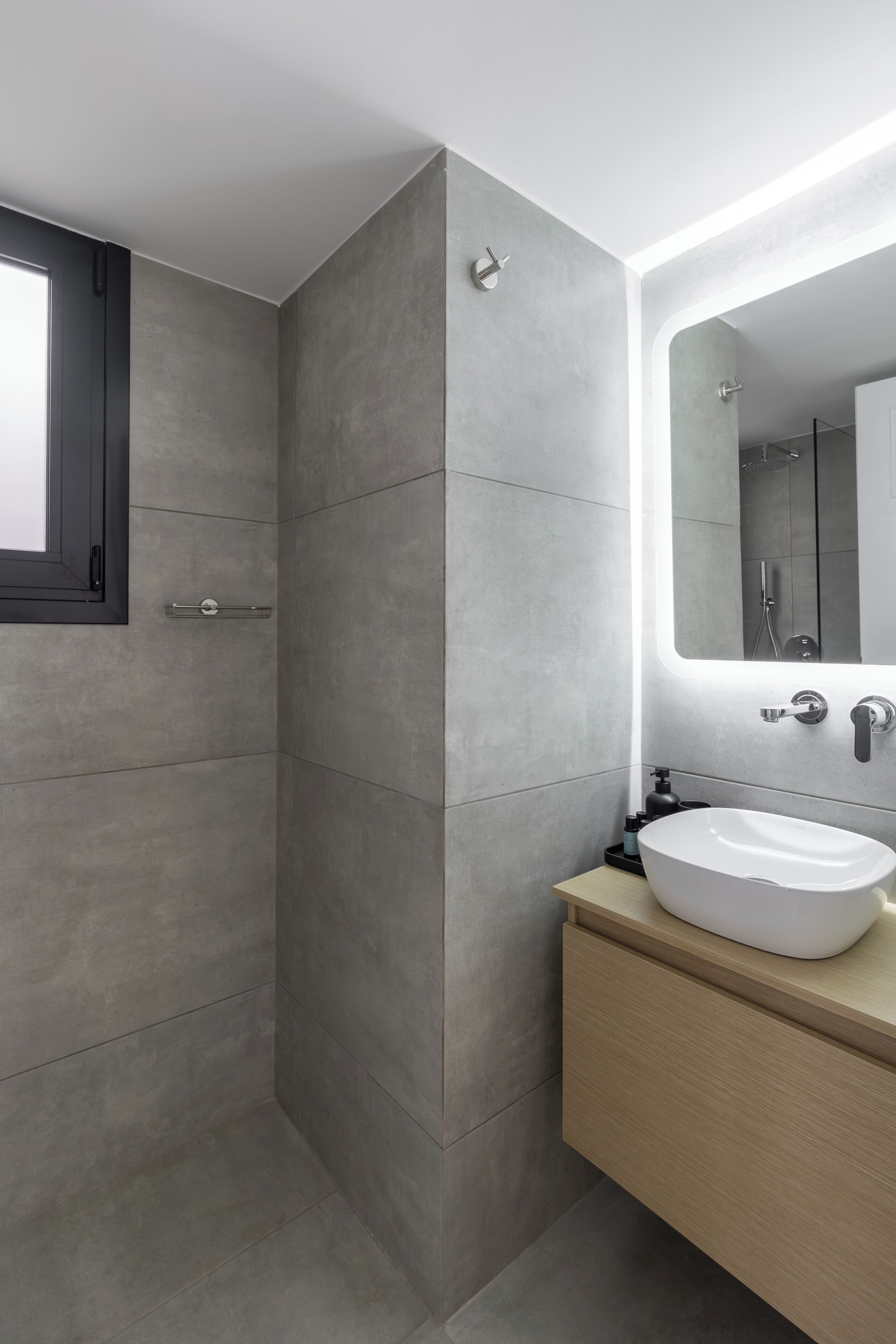 A modern bathroom with a walk-in shower, a large mirror, and a white sink.