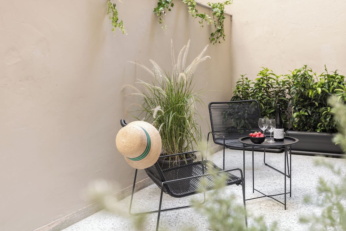 A small outdoor seating area with a metal chair, a table with a bottle and glasses, and a potted plant.