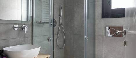 A modern bathroom with a glass-enclosed shower, a white sink, and a toilet.