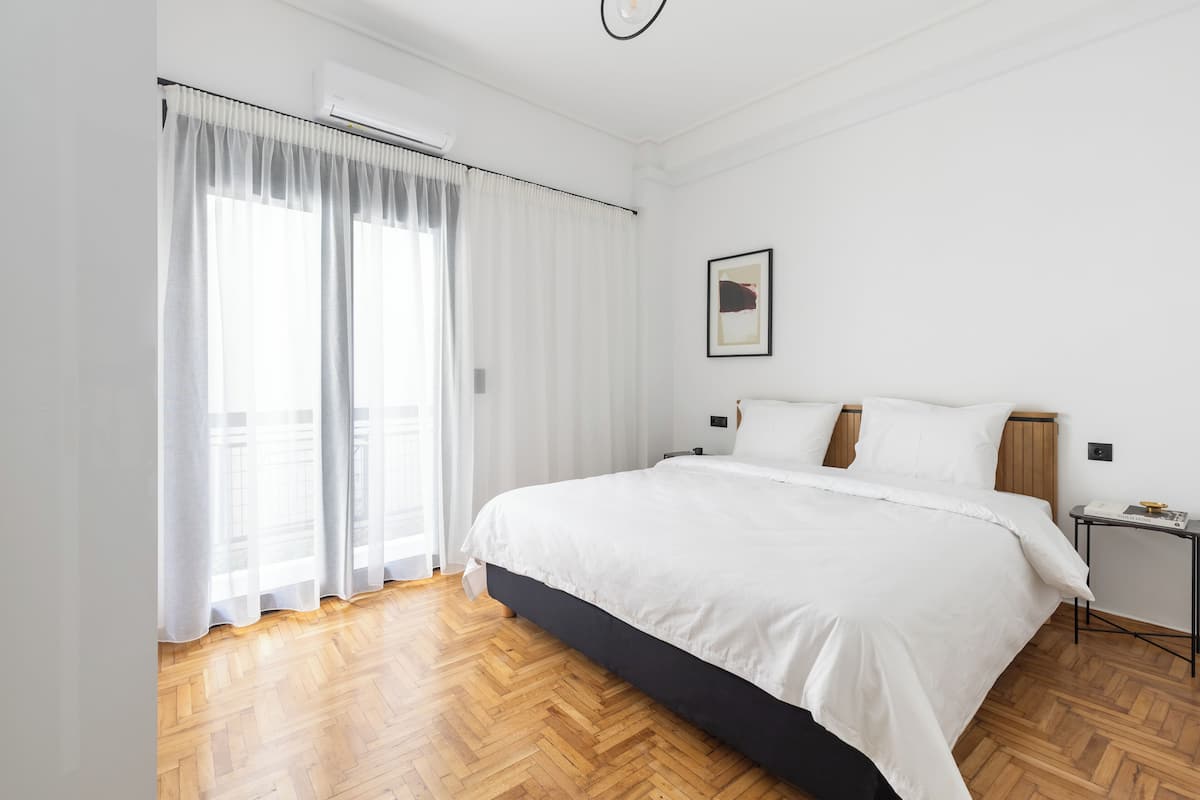 A modern bedroom with a large bed, a bedside table, and a window with sheer curtains.