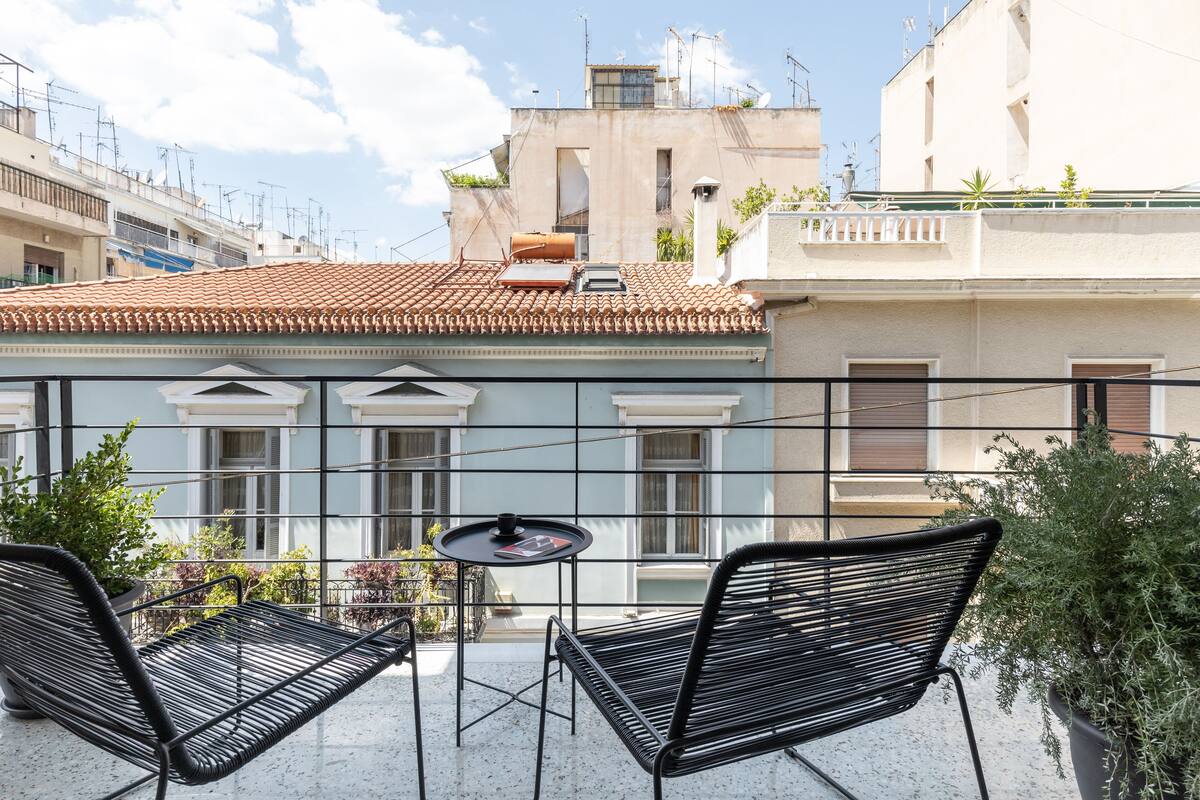 A balcony with two black metal chairs, a small round table, and a potted plant.