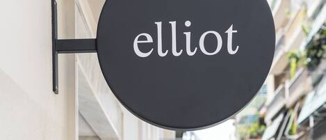 A circular sign with the word "elliot" mounted on a building facade.