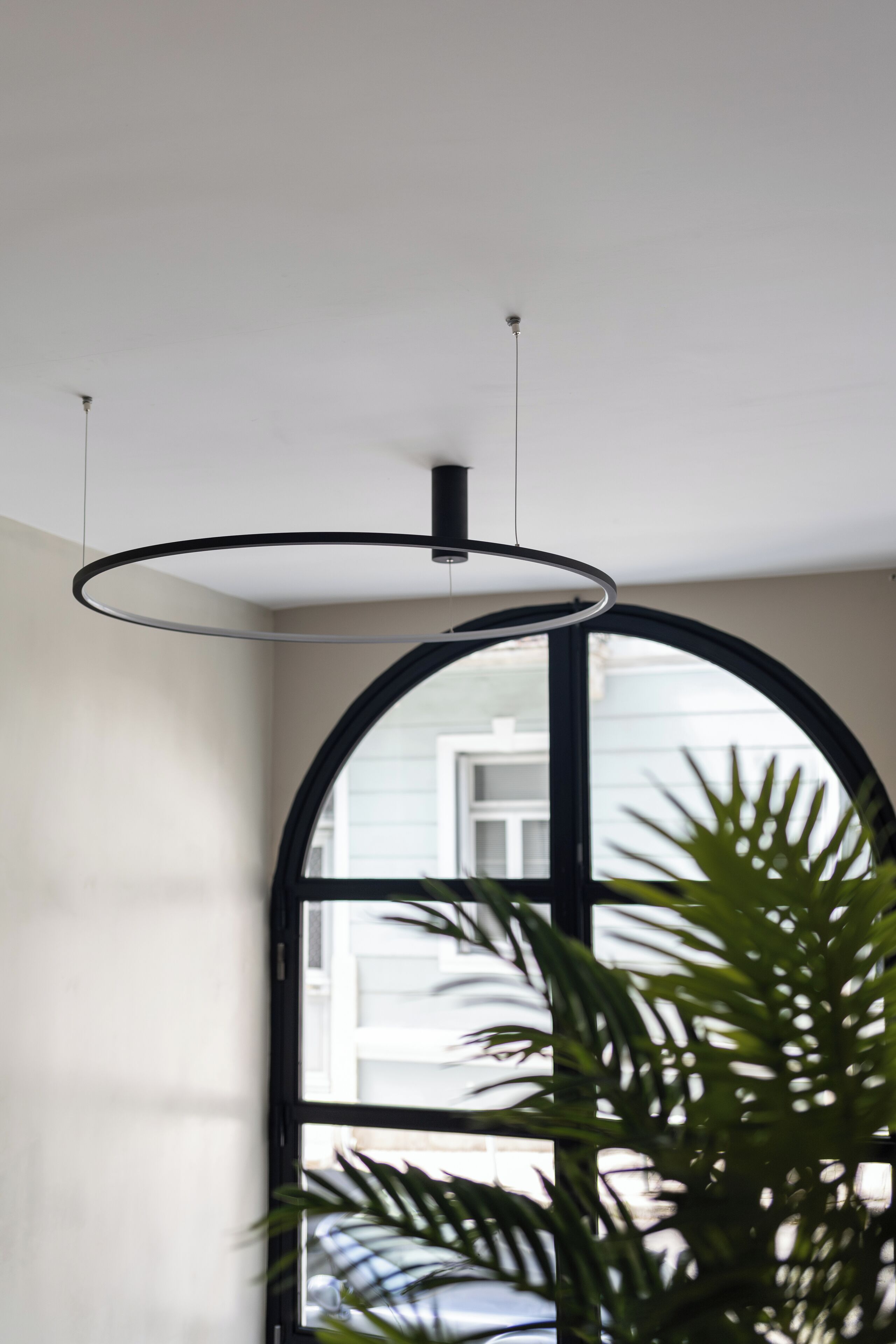 A modern interior with a circular ceiling light fixture, a large arched window, and a potted plant.