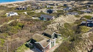 Ett flygbildsbild av en kustby med hus som är byggda på sanddyner, och som visar en blandning av traditionell och modern arkitektur.