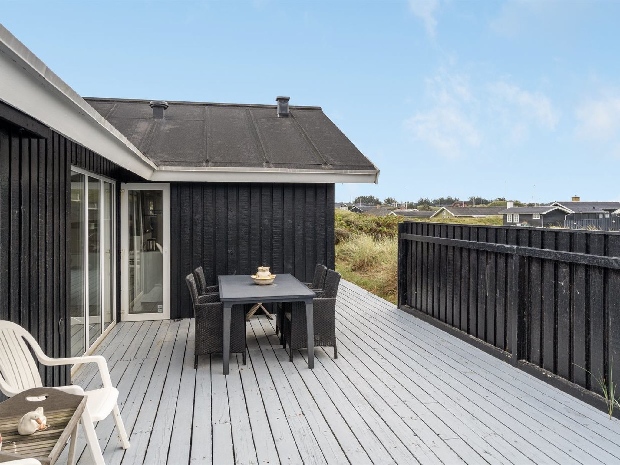 Une terrasse avec une table et des chaises, un petit chien blanc et une clôture noire.