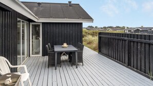 Une terrasse avec une table et des chaises, un petit chien blanc et une clôture noire.