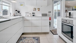 Une cuisine moderne avec des meubles blancs, un four encastré et une grande fenêtre qui laisse entrer la lumière naturelle.