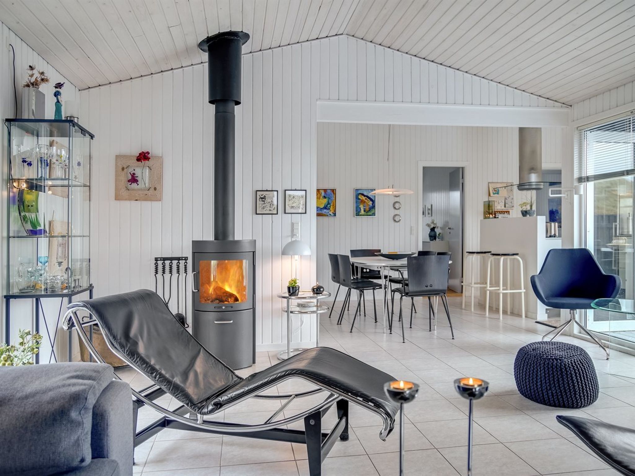 A modern living room with a wood-burning stove, a glass dining table, and a lounge chair.