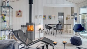 Un salon moderne avec un poêle à bois, une table à manger en verre et un fauteuil de relaxation.