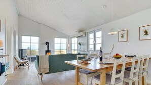 A spacious dining area with a wooden table and white chairs, a green cushioned bench, and a large window providing a view of the outdoors.