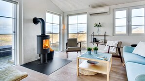 A modern living room with a wood-burning stove, large windows, a sofa, a coffee table, and a chair.