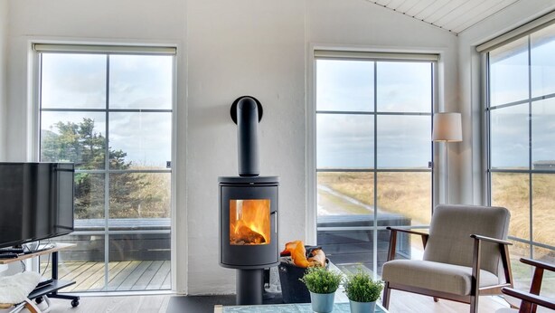 A modern living room with a wood-burning stove, large windows, a TV, and a comfortable seating area.