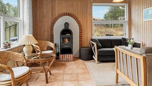 Habitació acollidora amb parets de fusta, una llar de foc, mobles de vimet i grans finestres que donen a l'exterior.