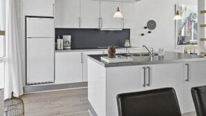 Een moderne keuken met witte kasten, een centraal eiland, hanglampen en een koffiezetapparaat.