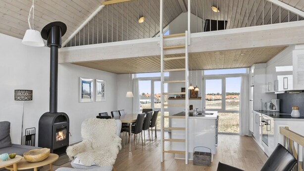 Een ruime woonkamer met een hoge plafond, een open haard, een eettafel met stoelen, en een keuken met een spoelbak en kastjes.