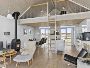Amplia sala de estar con techos altos, chimenea, mesa de comedor con sillas y zona de cocina con pileta y alacenas.