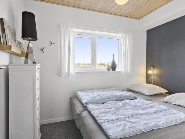 Un dormitorio con cama, mesita de noche, lámpara, ventana y vistas al exterior.