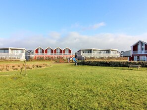 Une rangée de maisons de plage rouges et blanches, avec un champ verdoyant au premier plan.